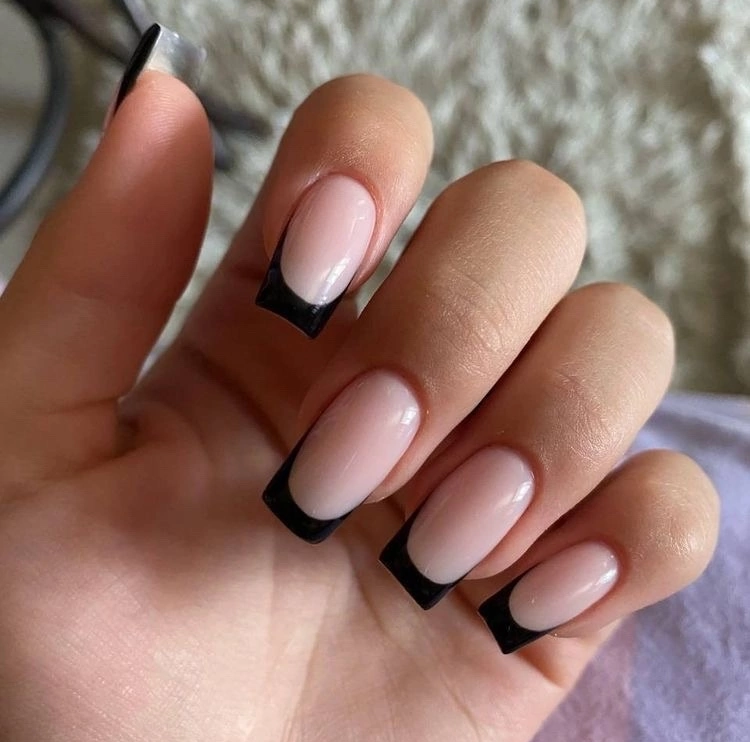 A close-up view of a hand showcasing a freshly done manicure with long, coffin-shaped nails featuring a nude base color with glossy black tips for a sophisticated and modern take on the Spring Nail Trends