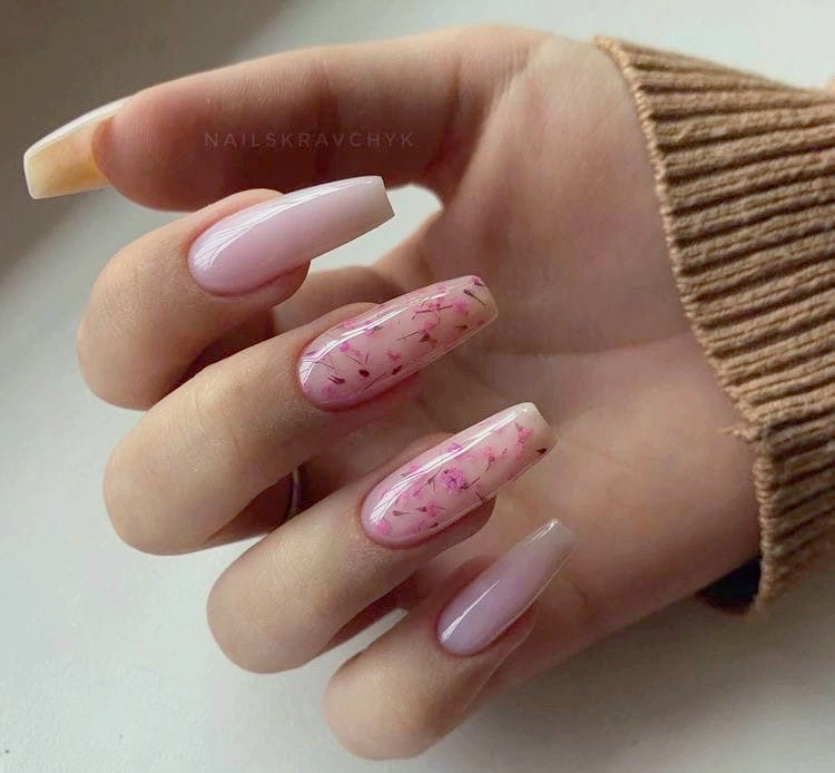 Elegant hand showcasing Spring Nail Trends 2024 with a manicure of long coffin nails, featuring a delicate pink base with subtle pink flower deign.