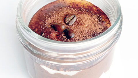 A delectable plant-based tiramisu oatmeal in a glass jar, topped with a dusting of cocoa powder and garnished with coffee beans.