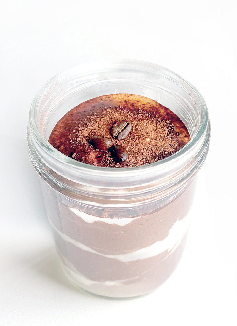 A delectable plant-based tiramisu oatmeal in a glass jar, topped with a dusting of cocoa powder and garnished with coffee beans.