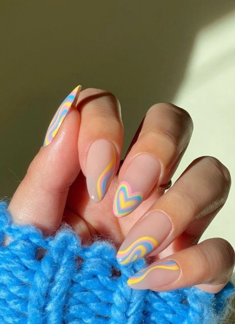 Artistically painted nails with rainbow wavy patterns and heart details, embodying Springtime Glamour, gently cradling a tuft of bright blue yarn, illuminated by a beam of sunlight.