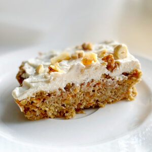 A slice of healthy low calorie carrot cake with ricotta cream topped with chopped nuts, served on a white plate