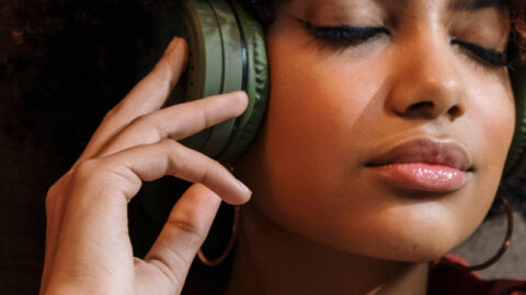 A young woman with curly hair enjoys guided meditation for sleep on her headphones, her eyes closed and a peaceful expression on her face, wearing a plaid shirt.