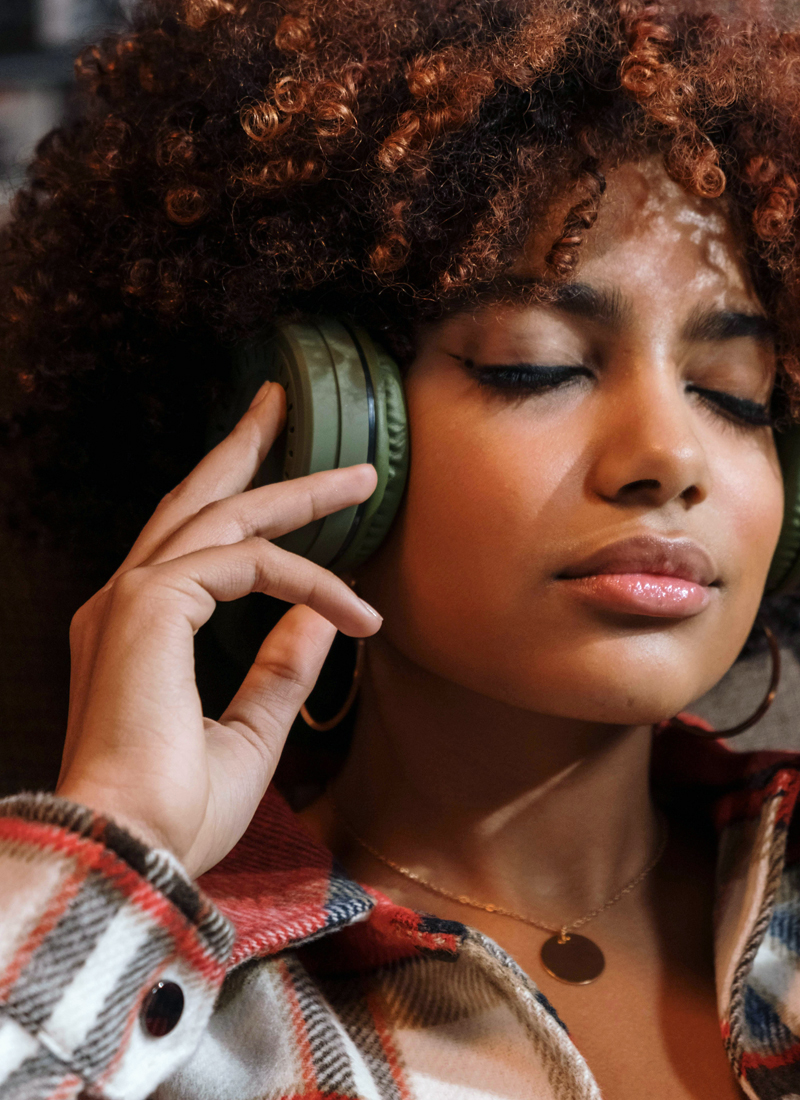 A young woman with curly hair enjoys guided meditation for sleep on her headphones, her eyes closed and a peaceful expression on her face, wearing a plaid shirt.