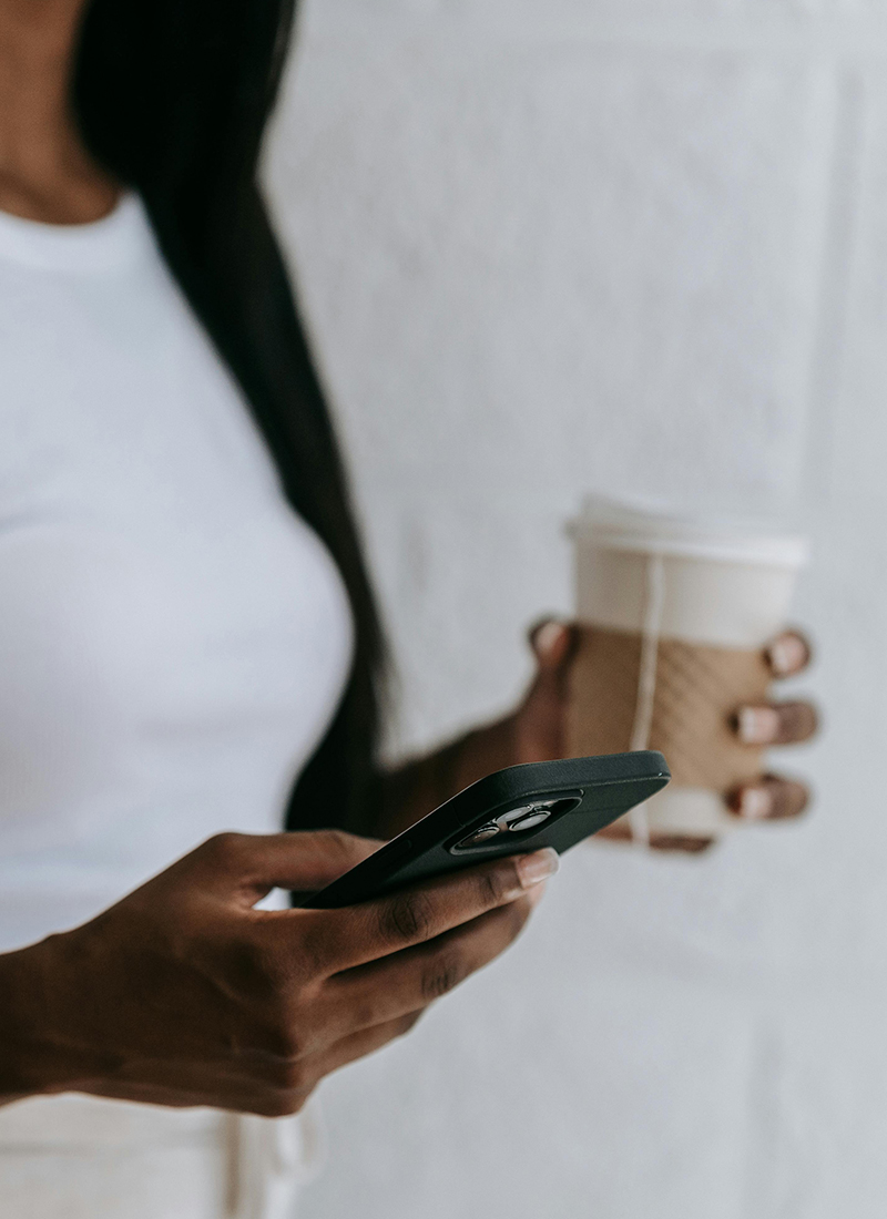 A person wearing a white shirt is holding a cup of coffee and a smartphone, presumably checking their task tracker app.